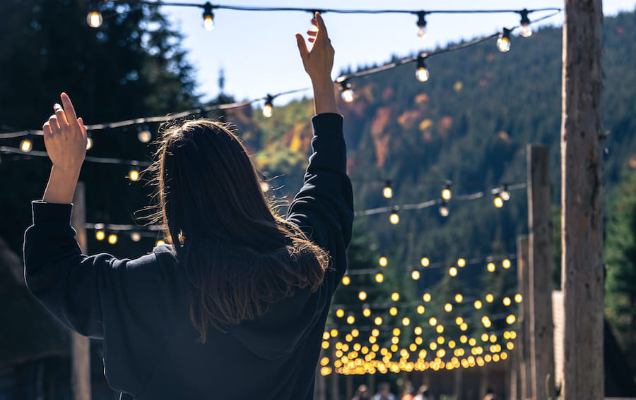 Использование влагозащищённой светодиодной гирлянды на солнечной батарее дает автономность от электросети и возможность перемещения светильников при смене сценария Девушка со спины с поднятыми руками, гирлянда, горный пейзаж