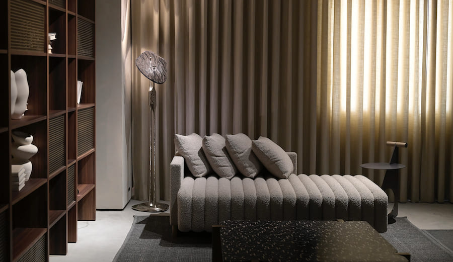 Пространство гостиной, диван - кровать с подушками, шкаф с книгами и арт объектами, окно со шторами, торшер