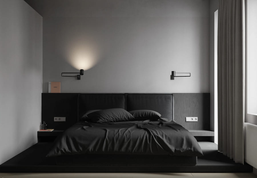 Чёрный металл доминирует в современных коллекциях. Бра выглядят строго и элегантно, создавая графичные акценты на светлых стенах Пространство спальни, кровать на подиуме, черный и серый текстиль, тумбочки, черные металлические бра, черные панели на стене