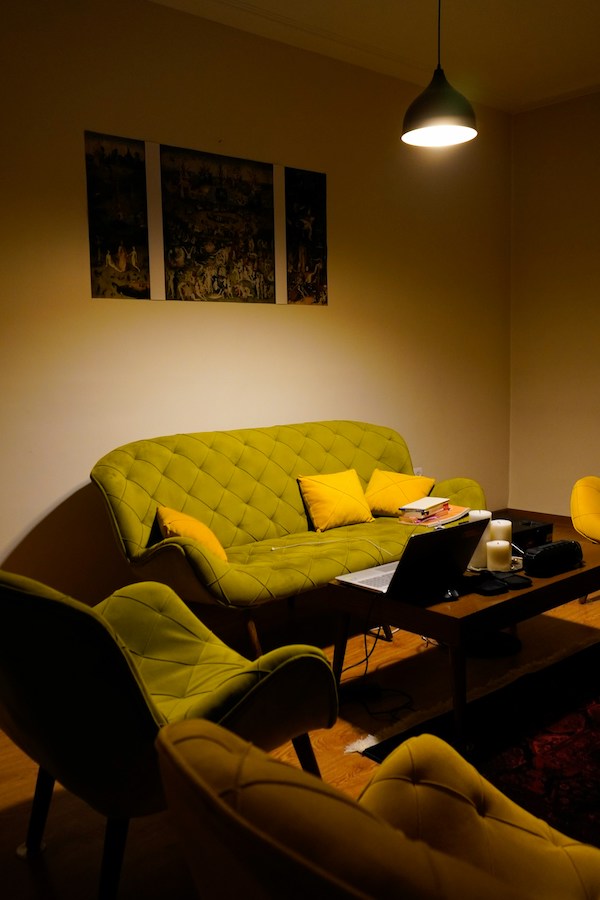 Темная комната, кушетка, мягкие стулья, журнальный стол с ноутбуком, яркий светильник