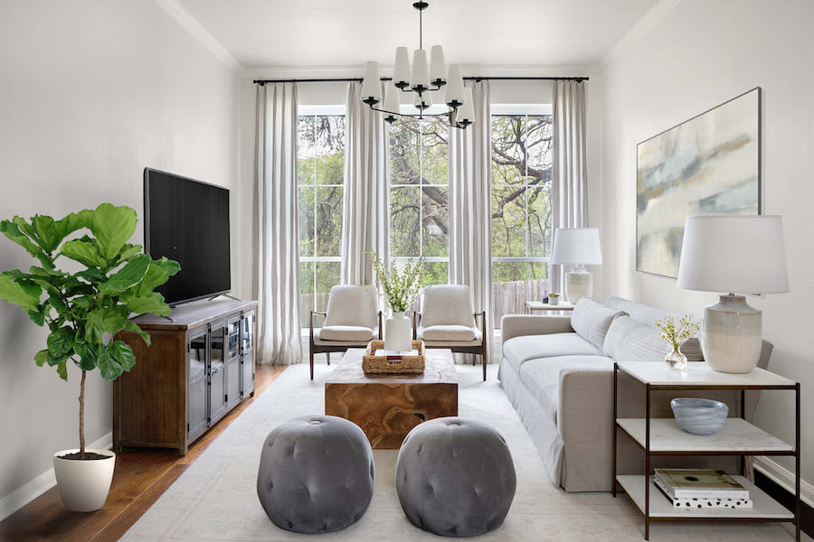 Пространство гостиной, панорамные окна, диван, два кресла, ТВ-панель на тумбочке, журнальный стол-куб, два пуфа, две этажерки с торшерами, растение в кашпо, картина на стене