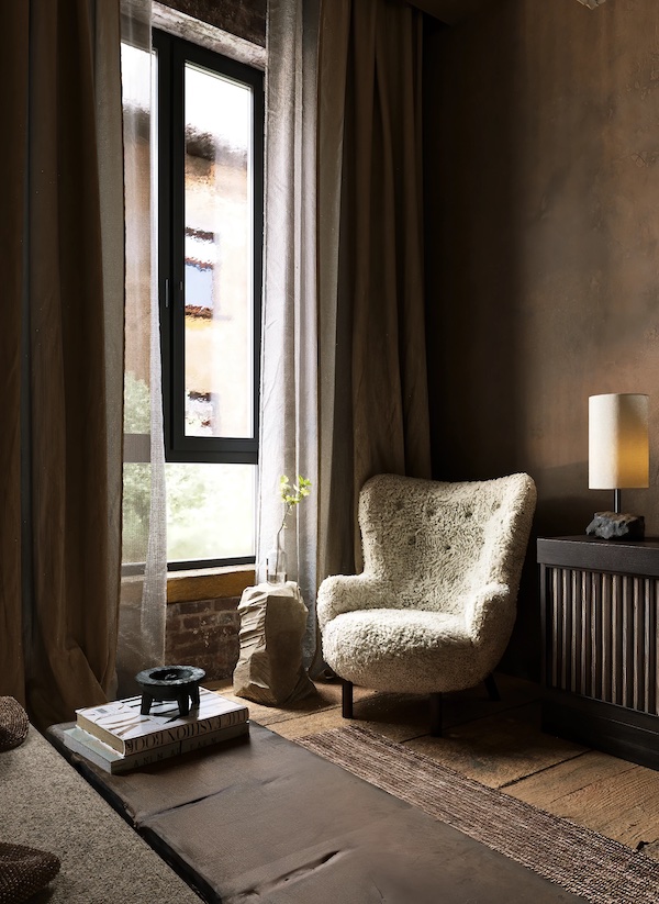 Угол комнаты, кресло, столик из камня, окно, настольная лампа, книги