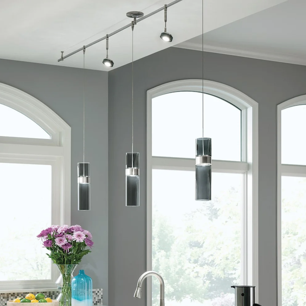Подвесные трековые светильники крепятся к шинопроводу с помощью тросов, источник света размещается на нужном уровне Подвесные трековые светильники на кухне, большие окна, ваза с цветами